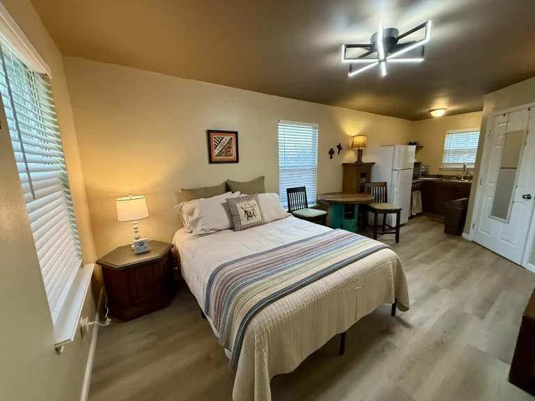 A dog friendly studio apartment in Garden City, TX, featuring a bed, a small dining table with chairs, and a kitchen area in the background.