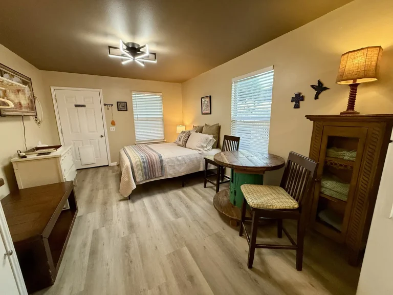 A furnished bedroom in a dog friendly cabin in Garden City, TX, featuring a bed, a round wooden table with a chair, and a cabinet.