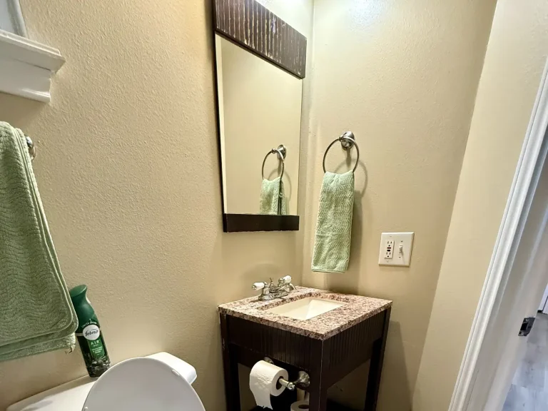 Small bathroom vanity with a speckled countertop, mirror, and two green towels in a dog friendly cabin in Garden City, TX.